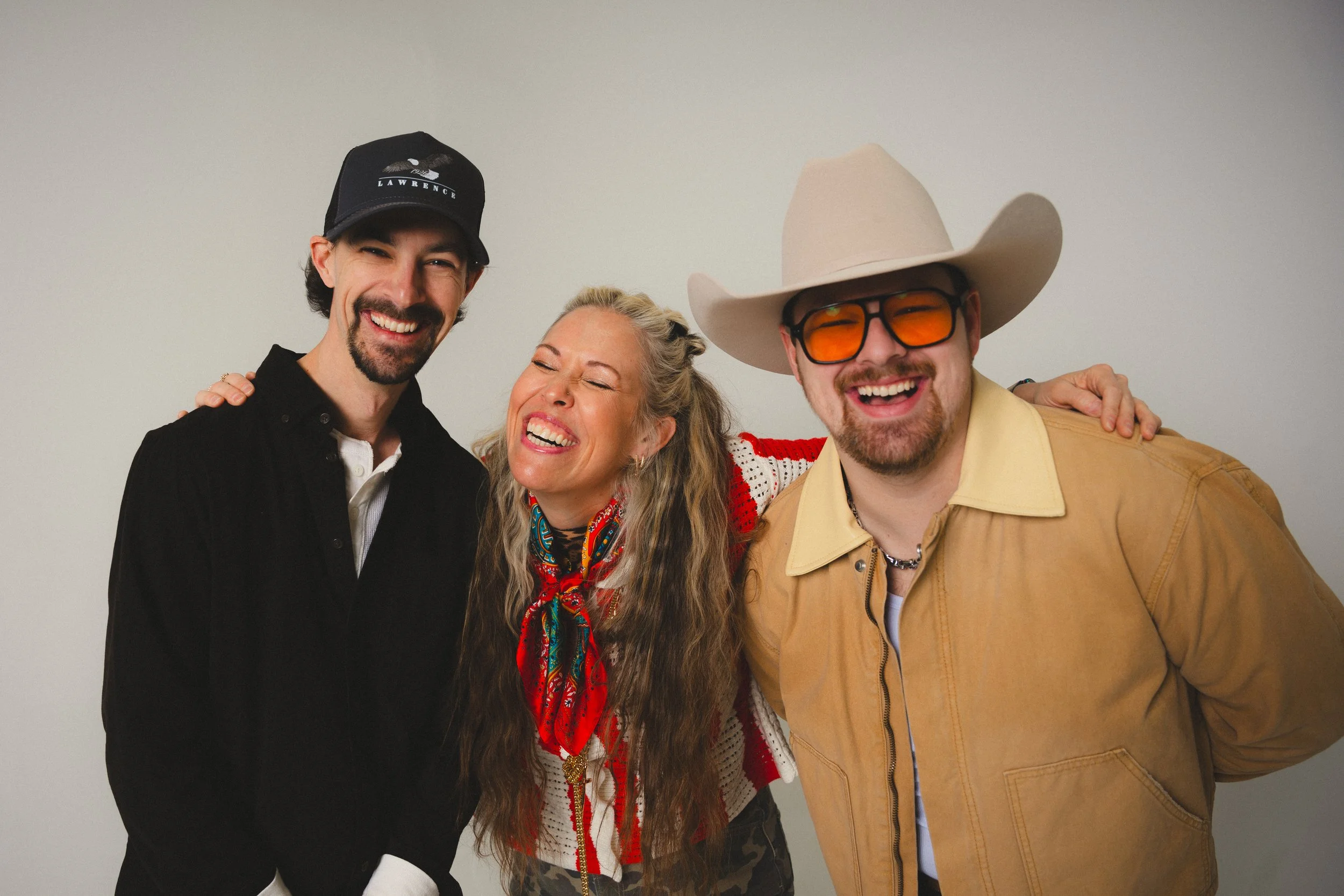 The three members of CLINE laughing together against a plain backdrop